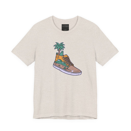 On the front of this custom handmade short sleeve shirt is an image of a high top running shoe with ocean waves running along the side of the shoe, coming out of the top of the shoe where your foot goes is a palm tree and a surf board.