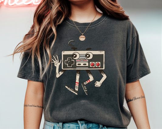On the front of this custom vintage gaming short sleeve shirt is an image of a old school Nintendo controller, the controller has arms and legs and a face that makes it look like a cartoon character.