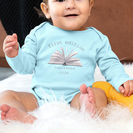 Baby wearing a light blue onesie with text and an open book graphic, sitting on a fluffy white surface.