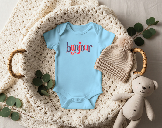 A custom infant onesie that has shirt sleeves and three buttons on the bottom, across the front of this custom baby bodysuit is the word bonjour in blue and red writing.