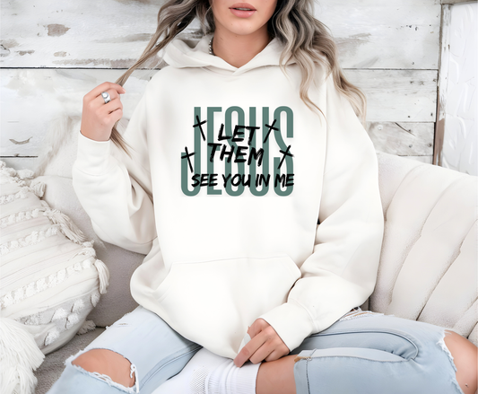 On the front of this custom Christian hoodie it says Jesus in large letters with the words Let them see you in me overlayed overtop of Jesus, there are crosses around the wording.
