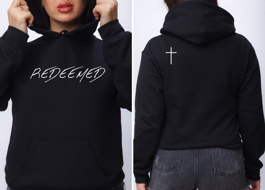 On the front of this custom Christian hoodie is the word Redeemed in a large modern font across the top of the sweater, on the back left shoulder blade there is a Jesus cross.