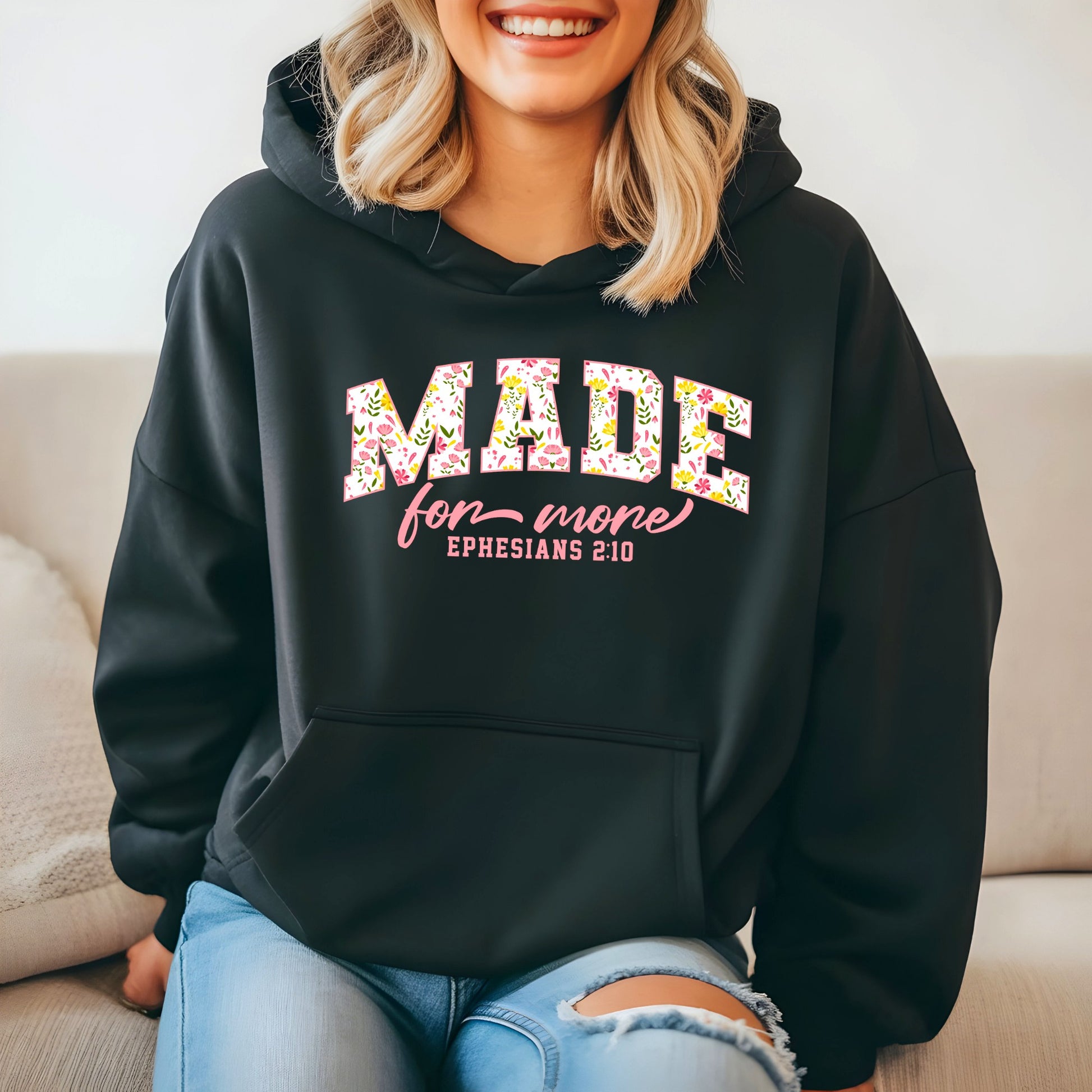 On the front of this custom Christian hoodie is the bible verse the says Made for more Ephesians 2:10, with the word "Made" being large block letters with a pink floral pattern inside the letters, all the other words are in a light pink color.