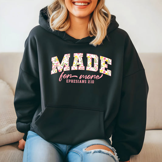 On the front of this custom Christian hoodie is the bible verse the says Made for more Ephesians 2:10, with the word "Made" being large block letters with a pink floral pattern inside the letters, all the other words are in a light pink color.