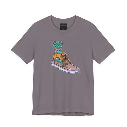 On the front of this custom handmade short sleeve shirt is an image of a high top running shoe with ocean waves running along the side of the shoe, coming out of the top of the shoe where your foot goes is a palm tree and a surf board.