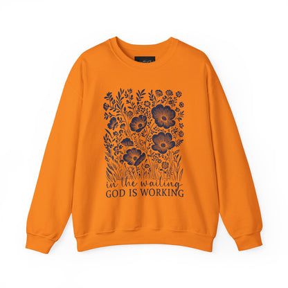 On the front of this custom women's Christian pullover sweatshirt are a bunch of wildflowers with the words in the waiting God is working underneath the flowers.
