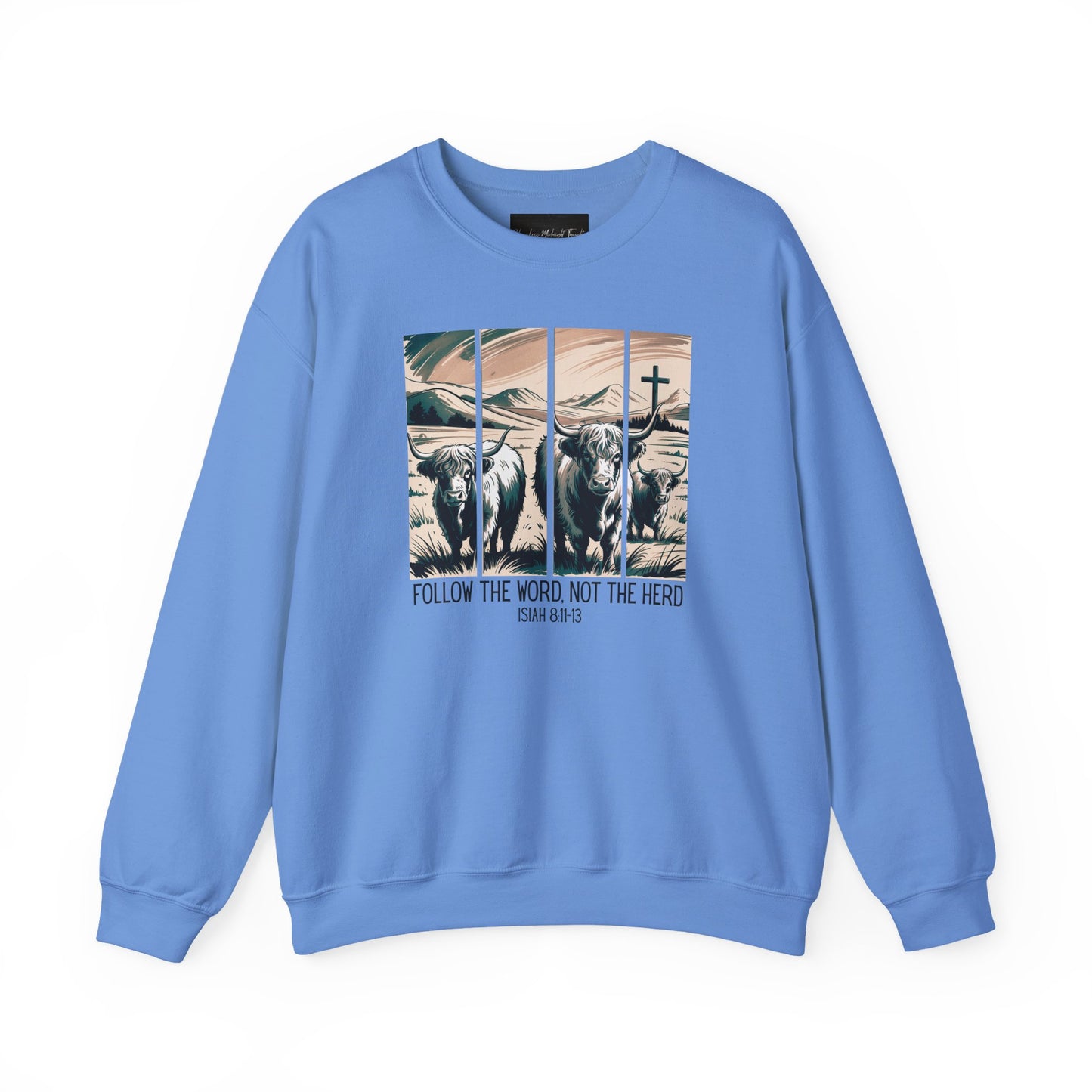 On the front of this Christian pullover sweatshirt is the image of cows standing in a pasture that is in a valley surrounded by mountains, there is a Jesus cross behind the cows, underneath the image is the scripture Follow the word, not the herd Isiah 8:11-13