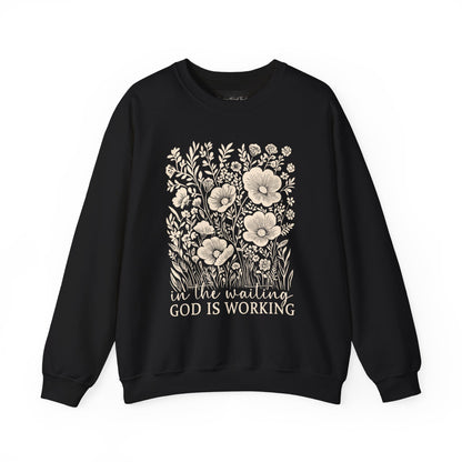 On the front of this custom women's Christian pullover sweatshirt are a bunch of wildflowers with the words in the waiting God is working underneath the flowers.