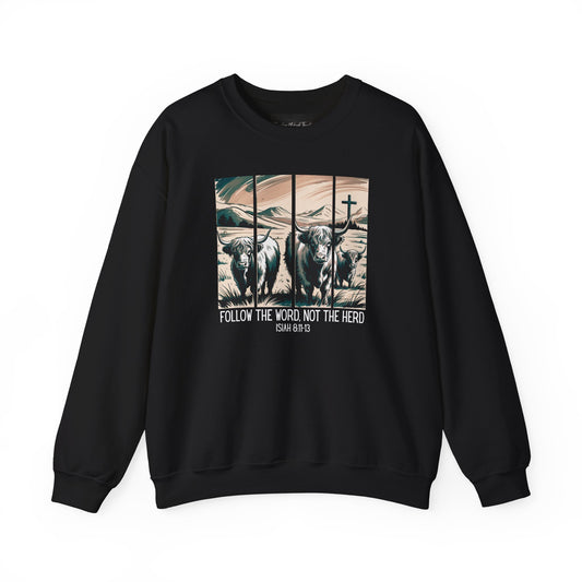 On the front of this Christian pullover sweatshirt is the image of cows standing in a pasture that is in a valley surrounded by mountains, there is a Jesus cross behind the cows, underneath the image is the scripture Follow the word, not the herd Isiah 8:11-13