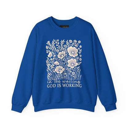 On the front of this custom women's Christian pullover sweatshirt are a bunch of wildflowers with the words in the waiting God is working underneath the flowers.