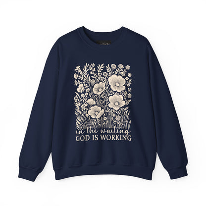 On the front of this custom women's Christian pullover sweatshirt are a bunch of wildflowers with the words in the waiting God is working underneath the flowers.