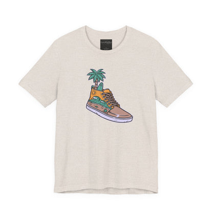 On the front of this custom handmade short sleeve shirt is an image of a high top running shoe with ocean waves running along the side of the shoe, coming out of the top of the shoe where your foot goes is a palm tree and a surf board.