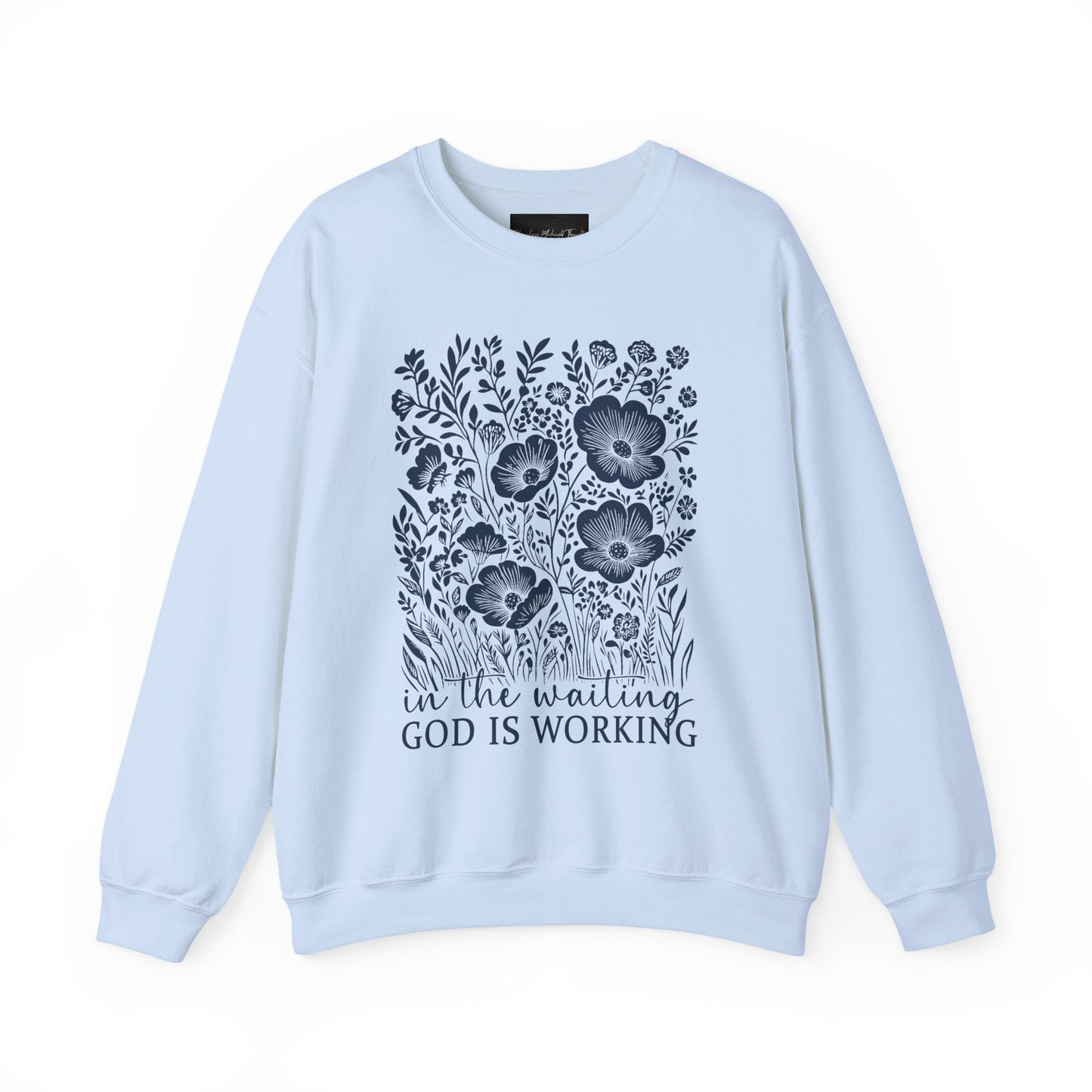 On the front of this custom women's Christian pullover sweatshirt are a bunch of wildflowers with the words in the waiting God is working underneath the flowers.