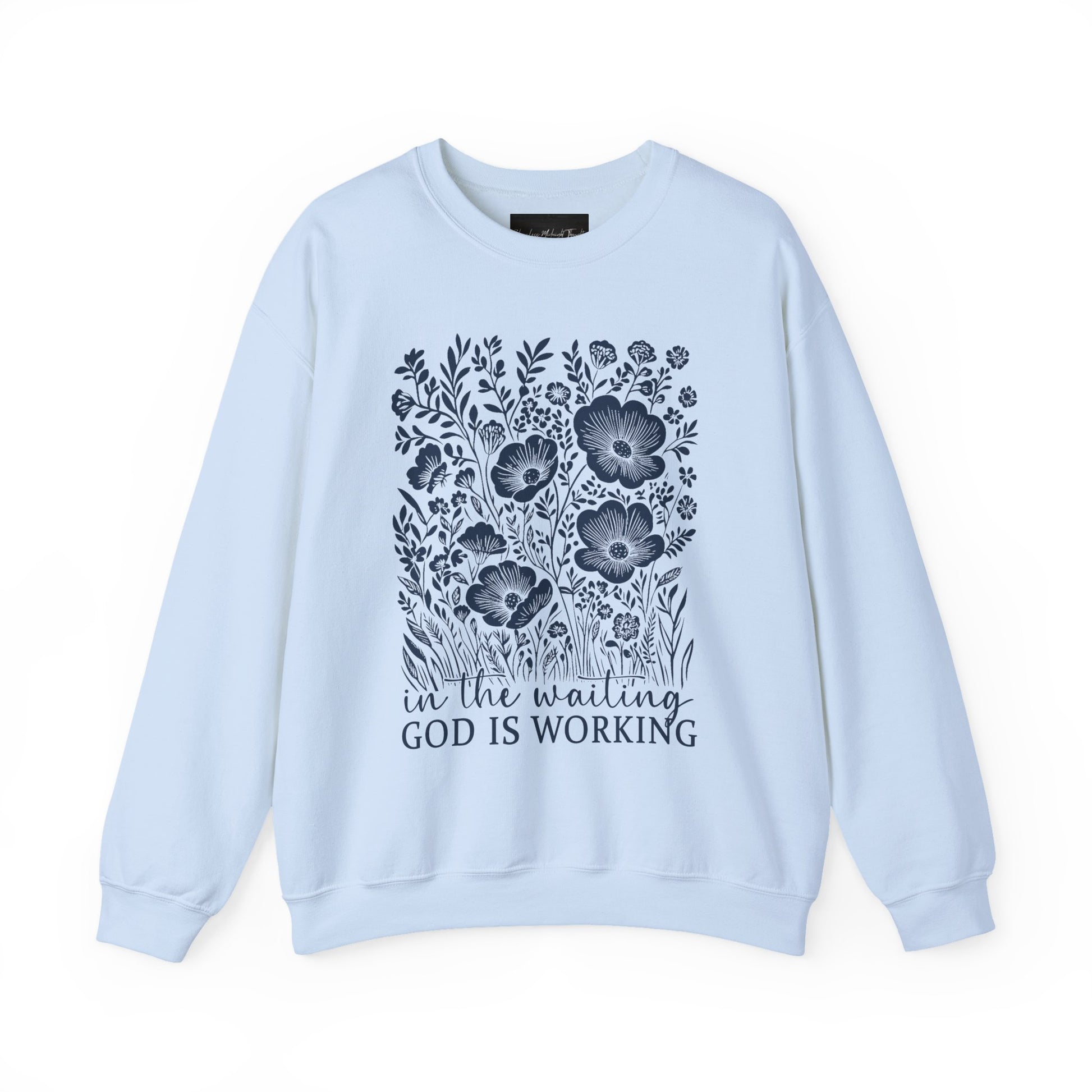 On the front of this custom women's Christian pullover sweatshirt are a bunch of wildflowers with the words in the waiting God is working underneath the flowers.