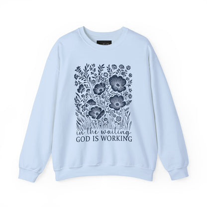 On the front of this custom women's Christian pullover sweatshirt are a bunch of wildflowers with the words in the waiting God is working underneath the flowers.