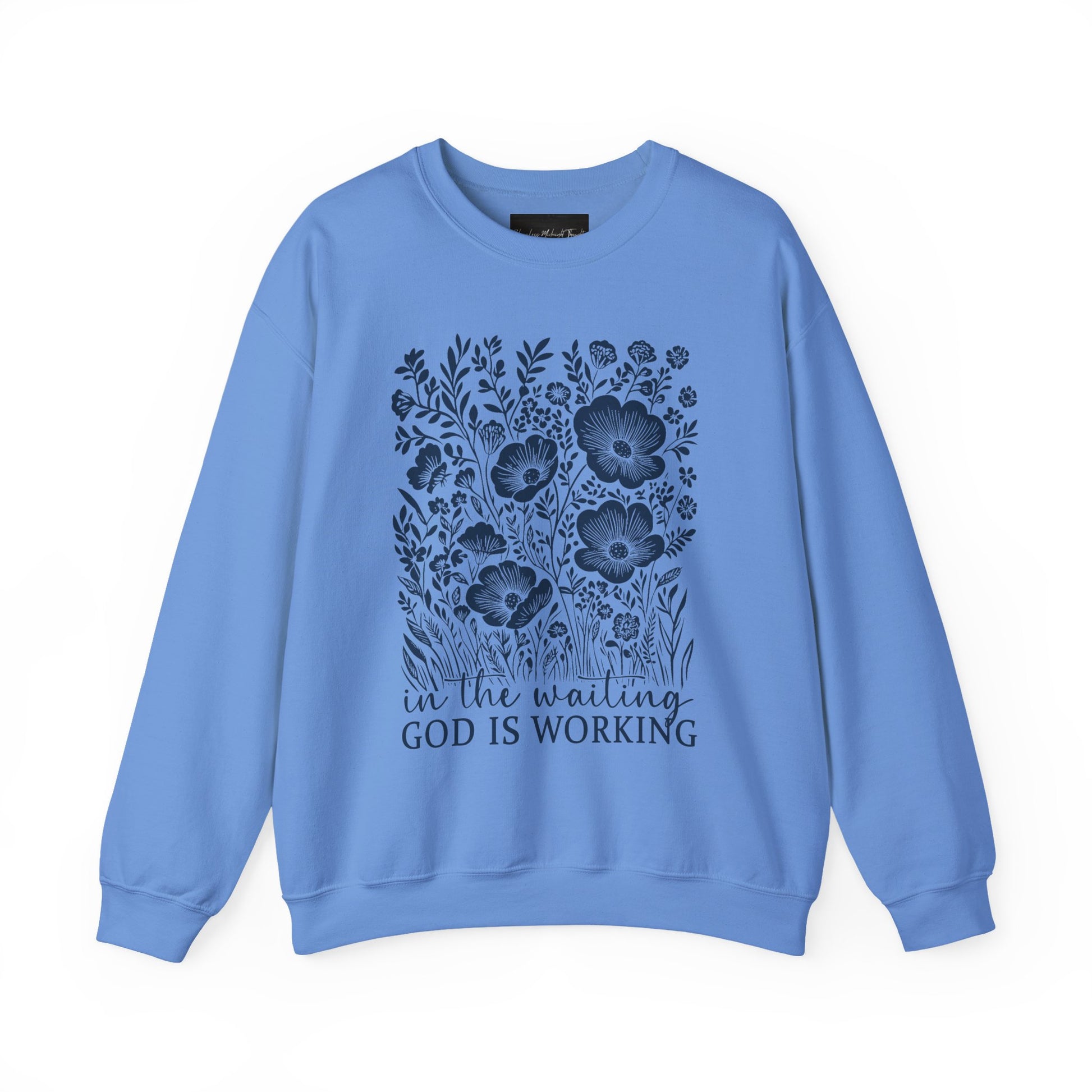 On the front of this custom women's Christian pullover sweatshirt are a bunch of wildflowers with the words in the waiting God is working underneath the flowers.