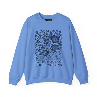 On the front of this custom women's Christian pullover sweatshirt are a bunch of wildflowers with the words in the waiting God is working underneath the flowers.