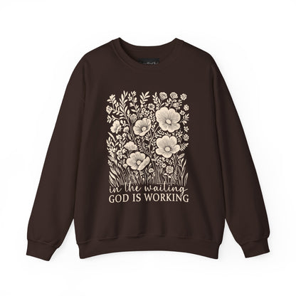 On the front of this custom women's Christian pullover sweatshirt are a bunch of wildflowers with the words in the waiting God is working underneath the flowers.