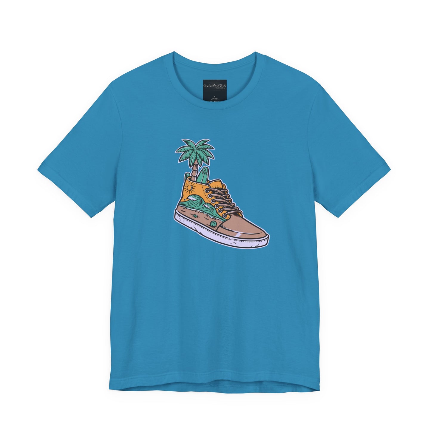 On the front of this custom handmade short sleeve shirt is an image of a high top running shoe with ocean waves running along the side of the shoe, coming out of the top of the shoe where your foot goes is a palm tree and a surf board.