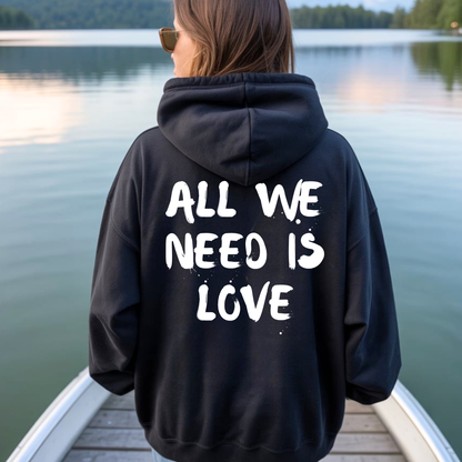 On the back of this custom unisex hoodie are the words all we need is love, the words look like they have been spray painted onto the sweater.