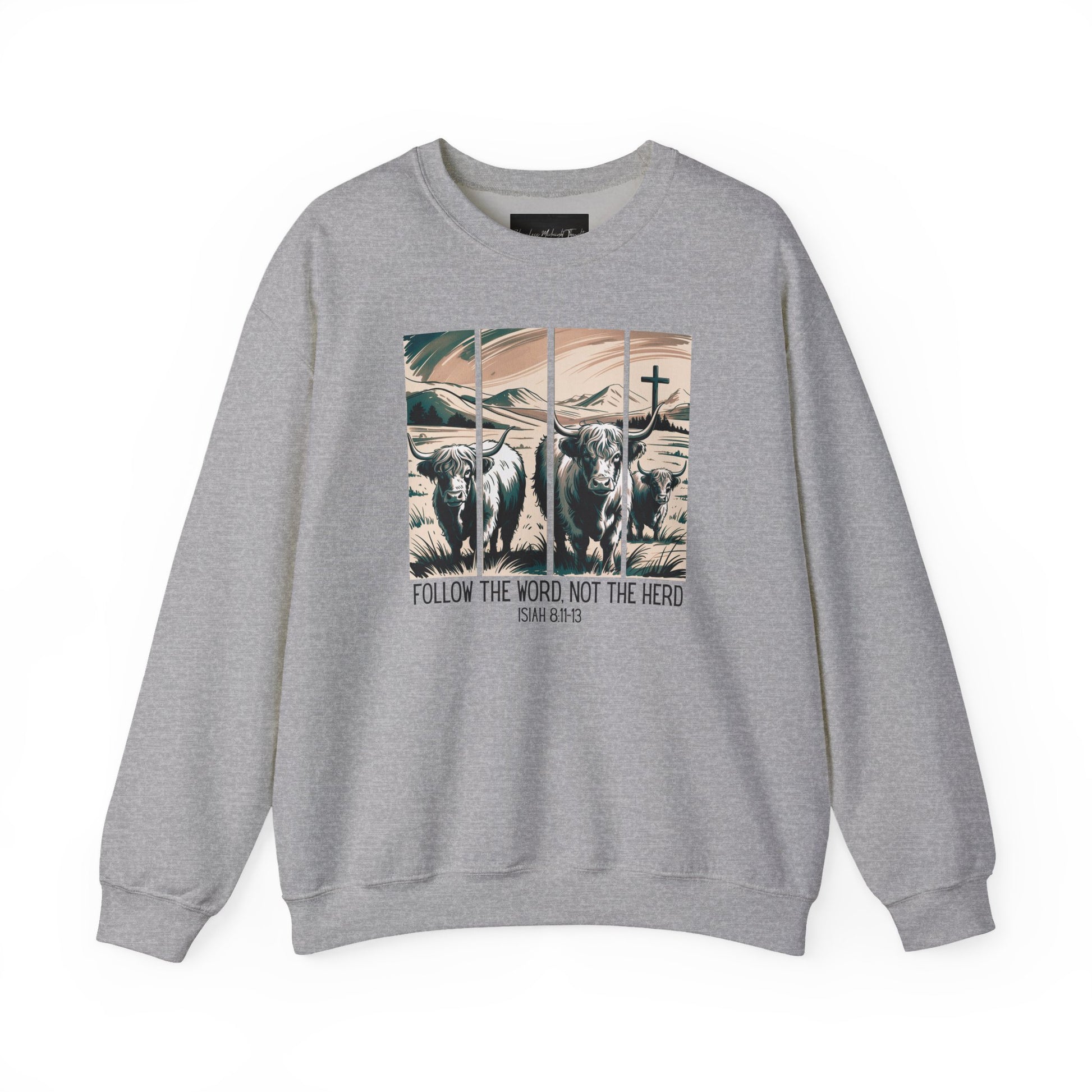On the front of this Christian pullover sweatshirt is the image of cows standing in a pasture that is in a valley surrounded by mountains, there is a Jesus cross behind the cows, underneath the image is the scripture Follow the word, not the herd Isiah 8:11-13