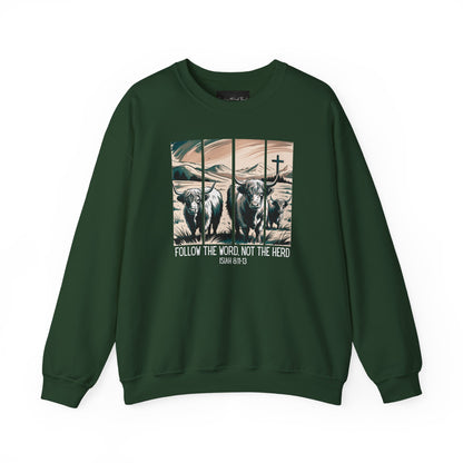 On the front of this Christian pullover sweatshirt is the image of cows standing in a pasture that is in a valley surrounded by mountains, there is a Jesus cross behind the cows, underneath the image is the scripture Follow the word, not the herd Isiah 8:11-13