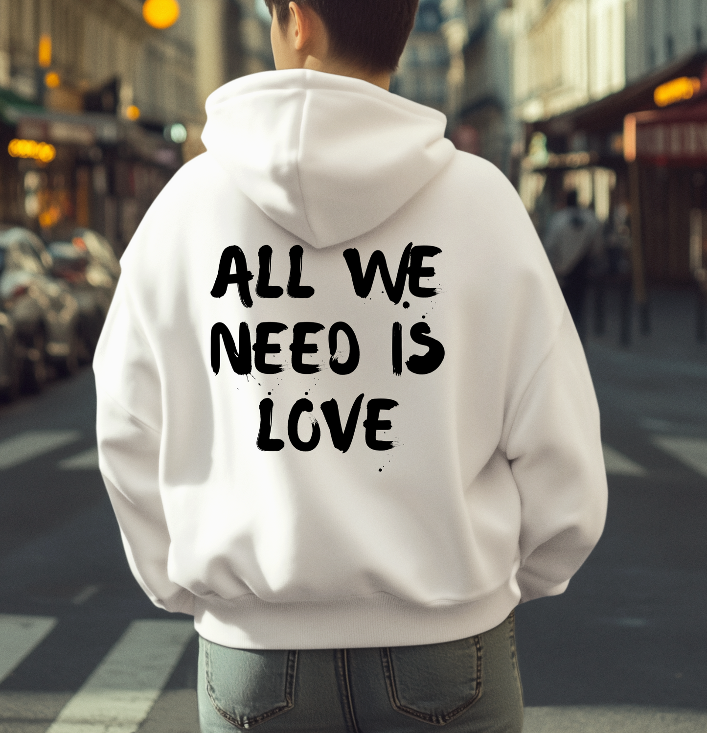 On the back of this custom unisex hoodie are the words all we need is love, the words look like they have been spray painted onto the sweater.