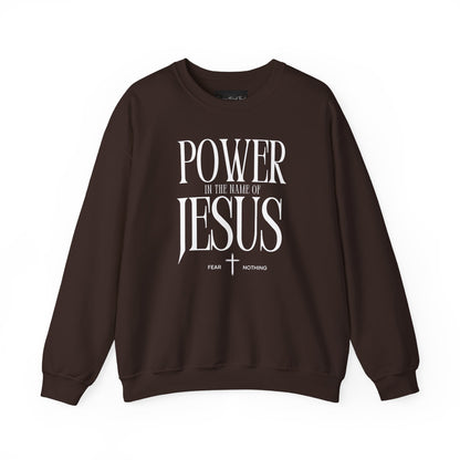 On the front of this Christian pullover sweatshirt it says Power In The Name Of Jesus with a Jesus cross underneath it, on either side of the cross are the words Fear and Nothing.