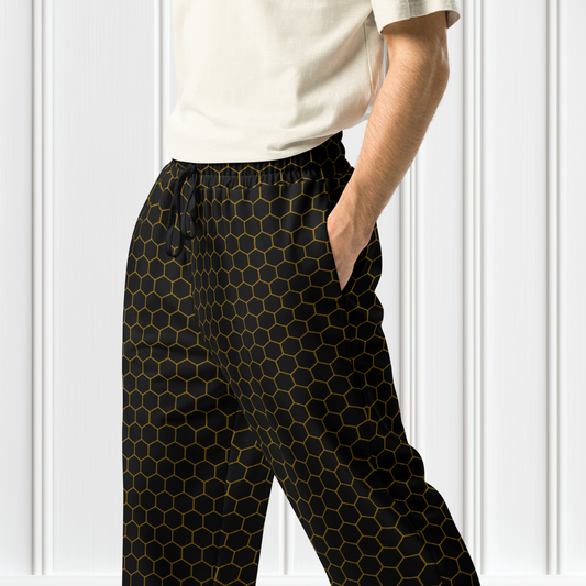 A pair of black wide leg unisex joggers featuring a gold honeycomb pattern. Perfect for lounging at home or working out at the gym. Ideal for those who love athleisure fashion. Great for casual wear during holidays and weekends.