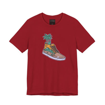 On the front of this custom handmade short sleeve shirt is an image of a high top running shoe with ocean waves running along the side of the shoe, coming out of the top of the shoe where your foot goes is a palm tree and a surf board.