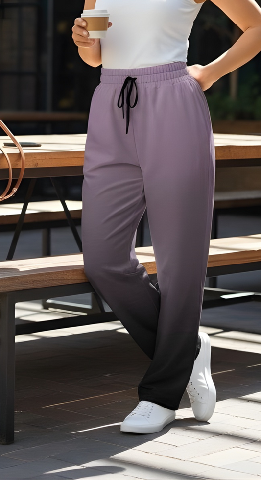 A pair of unisex wide leg joggers that have a ombre pattern starting with a lilac purple at the top then fading to a black at the bottom, the strings are black as well on this pair of pants.