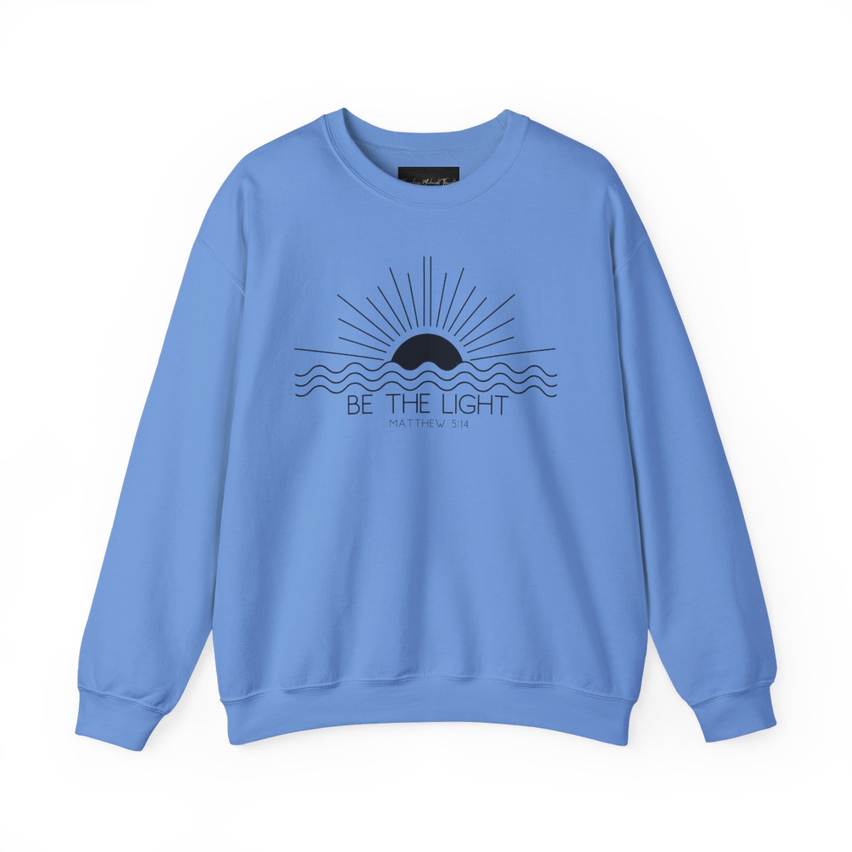 This cozy Christian crewneck sweatshirt features a sunrise over the ocean in the background with the bible verse Be the Light Matthew 5:14 in front of the image.
