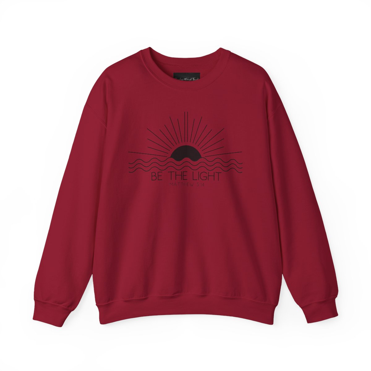This cozy Christian crewneck sweatshirt features a sunrise over the ocean in the background with the bible verse Be the Light Matthew 5:14 in front of the image.