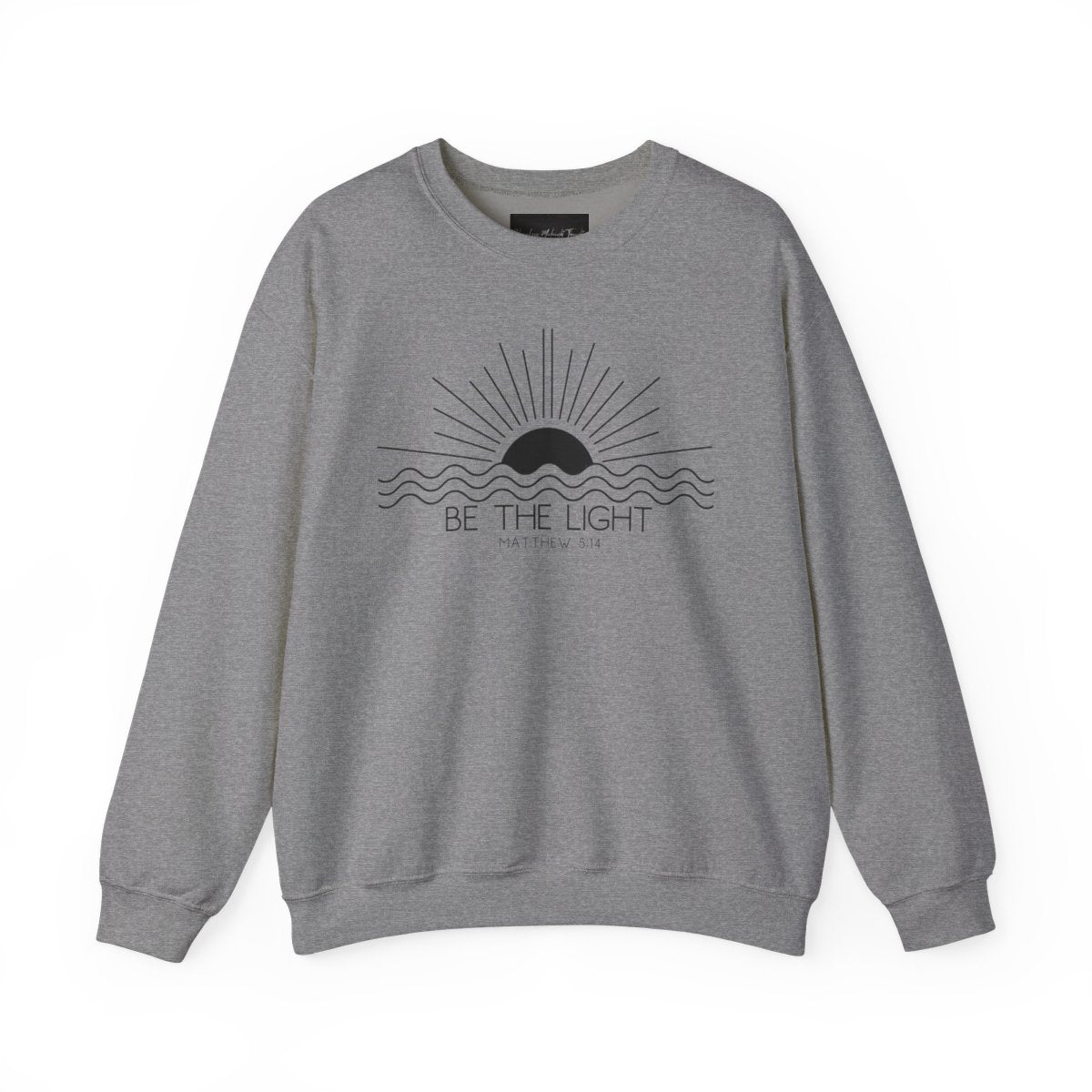 This cozy Christian crewneck sweatshirt features a sunrise over the ocean in the background with the bible verse Be the Light Matthew 5:14 in front of the image.