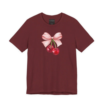 On the front of this custom women's short sleeve shirt is an image of a pair of cherries hanging from a stem with a pink bow on the top of them.