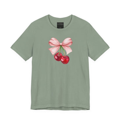 On the front of this custom women's short sleeve shirt is an image of a pair of cherries hanging from a stem with a pink bow on the top of them.