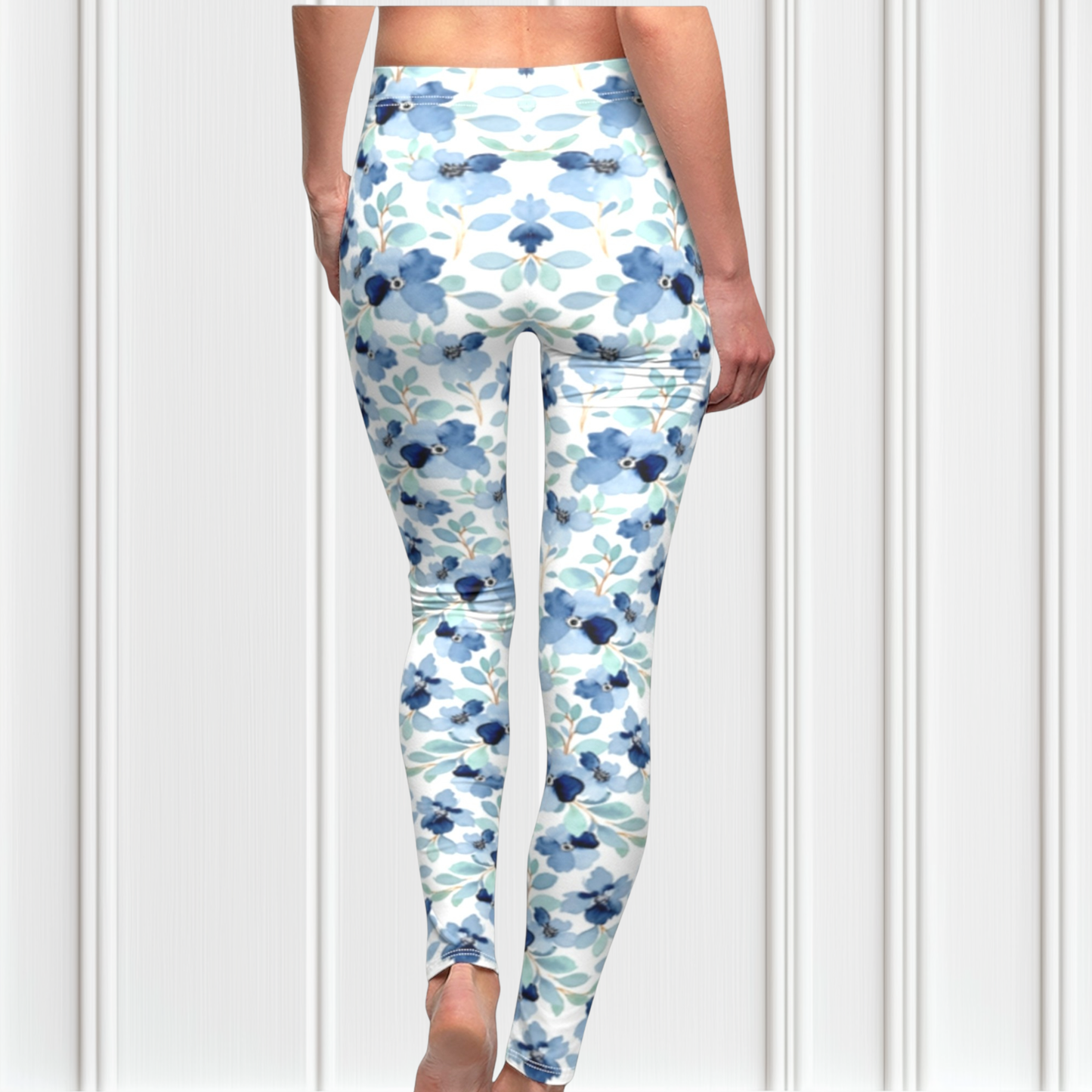 A pair of custom handmade high waisted women's leggings that are white and have a blue floral pattern with green leaves all over the pants.