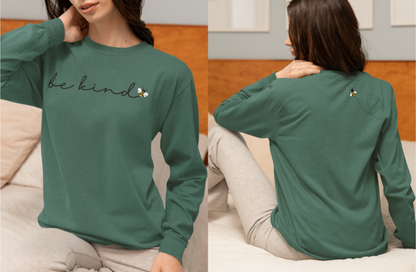 On the front of this custom unisex long sleeve shirt are the words be kind in a simple cursive font, with a bumble bee on the right side of the letter kind, on the back right shoulder there is an image of a bumble bee flying and leaving a trail behind it in the shape of a heart.