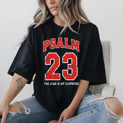 May include: Dark gray t-shirt with the text "PSALM 23" in red block letters above the number "23" in red. Below the number is the text "THE LORD IS MY SHEPHERD" in white. The shirt is a casual style.