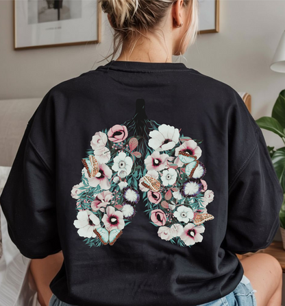On the back of this women's pullover sweatshirt is an image of a set of lungs, but the lungs are made out of vines with pink and white flowers all over them, there are butterflies sitting in top of the flowers that are light blue in color.