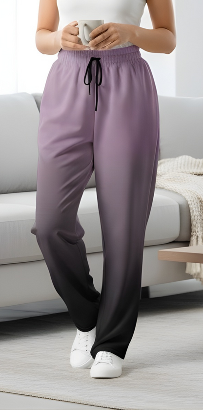 A pair of unisex wide leg joggers that have a ombre pattern starting with a lilac purple at the top then fading to a black at the bottom, the strings are black as well on this pair of pants.
