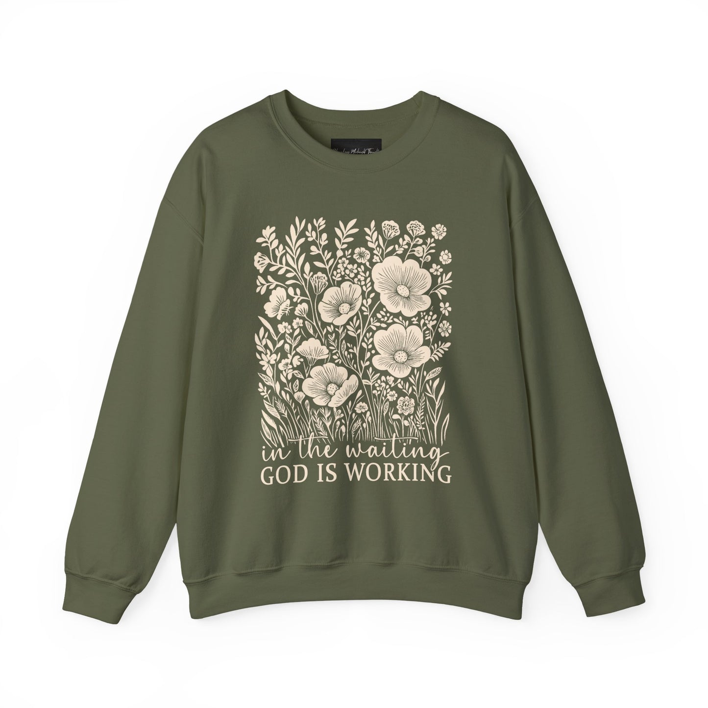 On the front of this custom women's Christian pullover sweatshirt are a bunch of wildflowers with the words in the waiting God is working underneath the flowers.