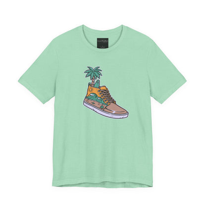 On the front of this custom handmade short sleeve shirt is an image of a high top running shoe with ocean waves running along the side of the shoe, coming out of the top of the shoe where your foot goes is a palm tree and a surf board.