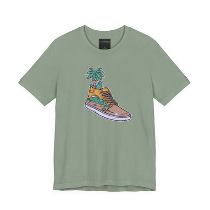 On the front of this custom handmade short sleeve shirt is an image of a high top running shoe with ocean waves running along the side of the shoe, coming out of the top of the shoe where your foot goes is a palm tree and a surf board.