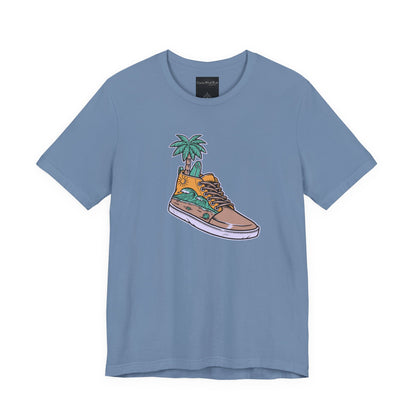 On the front of this custom handmade short sleeve shirt is an image of a high top running shoe with ocean waves running along the side of the shoe, coming out of the top of the shoe where your foot goes is a palm tree and a surf board.