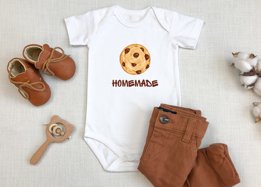 This adorable custom super soft baby onesie that features an image of a chocolate chip cookie in the middle with the word 'homemade' in brown writing underneath the image.