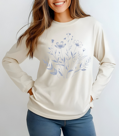 On the front of this custom women's long sleeve t-shirt is a image of a bunch of wildflowers and leaves coming from the bottom of the shirt to the very top, the flowers and leaves are in a light blue color.