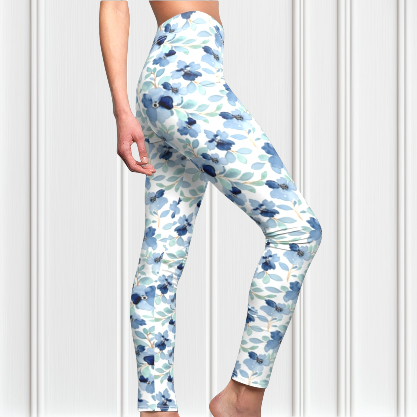A pair of custom handmade high waisted women's leggings that are white and have a blue floral pattern with green leaves all over the pants.