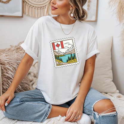 On the front of this custom Canadian pride short sleeve shirt is an image of a Canadian postage stamp with the Canadian flag in one corner and an image of mountains, a lake, and trees the make up the rest of the stamp.