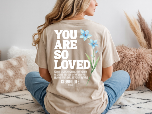 On the back of this Christian custom unisex t-shirt are the words You are loved in large bubble letters with a blue wildflower next to the words, the bible scripture John 3:16 is underneath that reads For God so loved the world that he gave his only son, so that whoever believes in him shall not perish but have everlasting life.